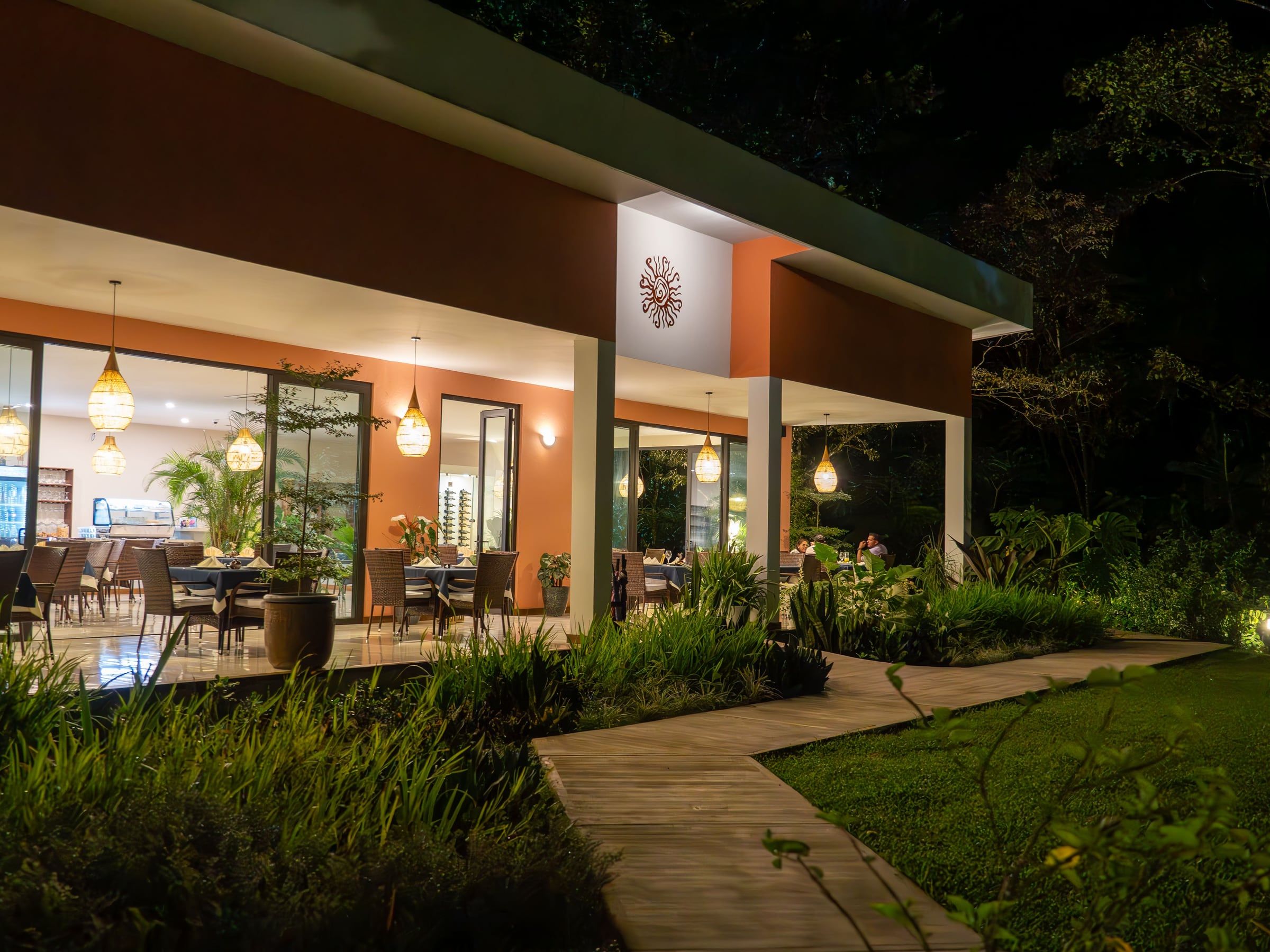 Fachada nocturna de Yan's Bistro con sendero de madera y jardín iluminado en Horquetas de Sarapiquí, Ruta 4